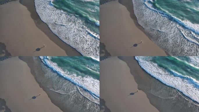 英国南部沿海海滩的空中无人机视图，冲浪者沿着海滩散步