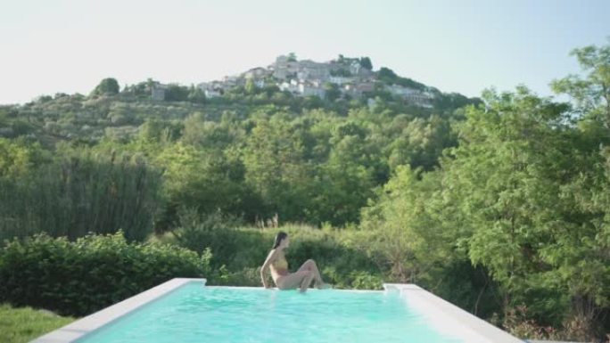 年轻女子在大自然的游泳池中游泳，俯瞰一个小村庄