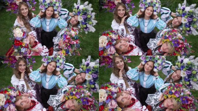 顶视图迷人的乌克兰年轻女性戴着花圈和民族服装抬头看着相机微笑。在夏季春季公园摆姿势的美丽女士的高角度