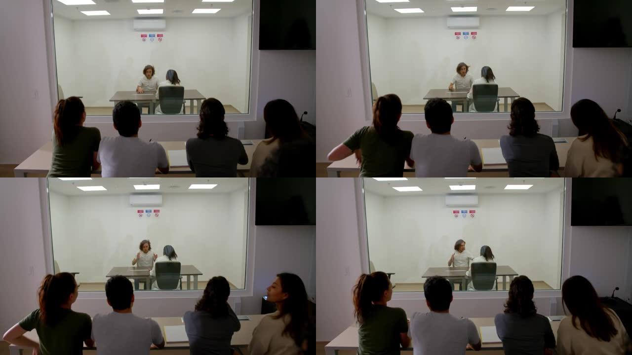 男病人在格塞尔室内接受女心理学家的采访，而其他学生在另一边观察