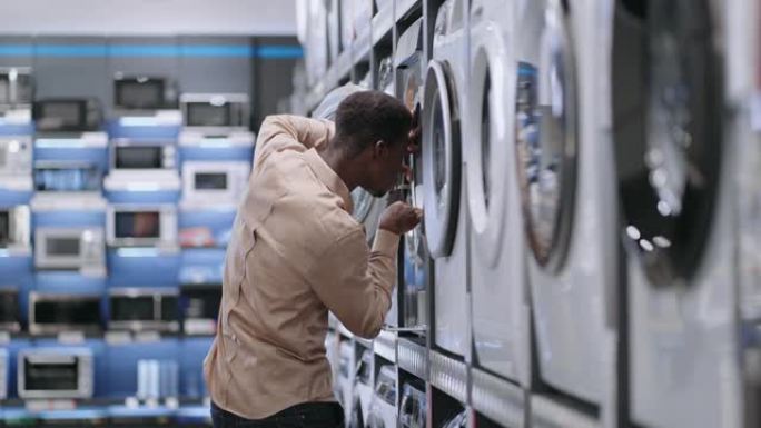 单身非裔美国人在家电商店选择洗衣机，男人在看展览样品