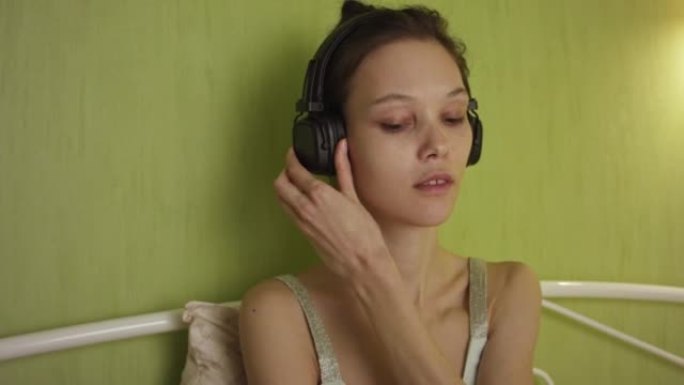 年轻女子在卧室里坐在床上时使用黑色蓝牙耳机。