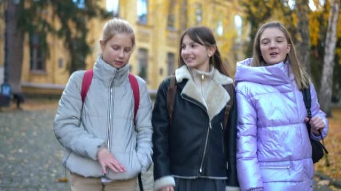 追踪三个积极的女性青少年同学课后闲聊的镜头。美丽快乐的高加索女学生在校园里散步。实时摄像机跟随学生。