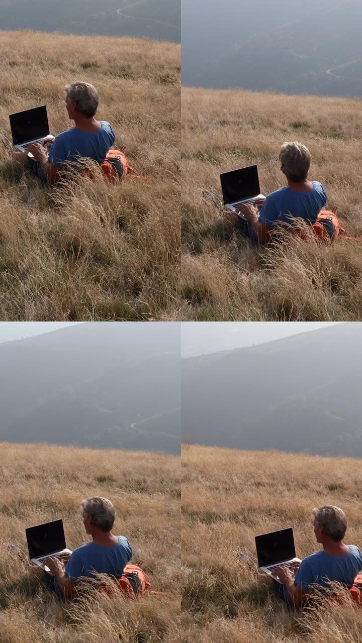 男子在山区草草草地上使用笔记本电脑