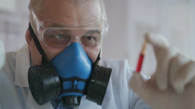 一位科学家戴着蓝色呼吸器和防护眼镜的极端特写镜头，这是一种冠状病毒疫苗的开发者，手持红色安瓿。医生看