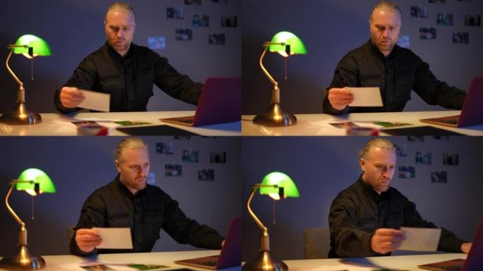 自信认真的警察坐在桌子旁，用笔记本电脑比较照片思考。集中职业警察在警察局调查犯罪案件的肖像。