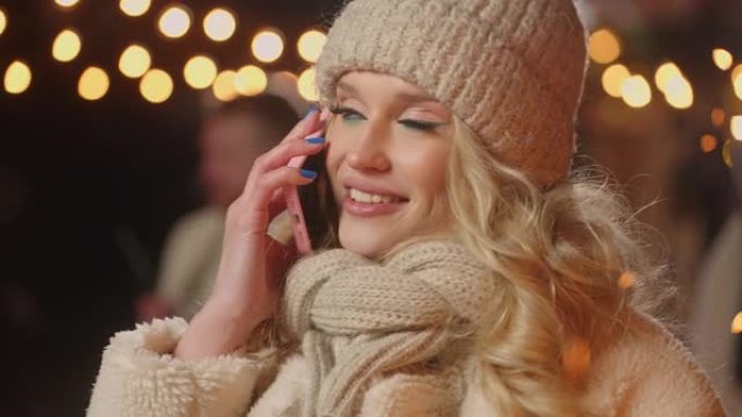美丽的女人在圣诞节或新年之夜从城镇广场通过手机打电话，特写肖像