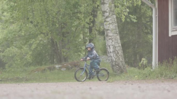 慢动作-一个年幼的孩子在大雨中骑自行车