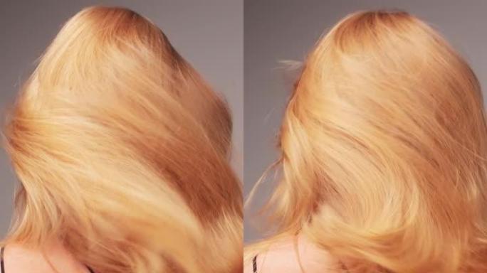 美丽诱人的金发女人在白色背景上向相机展示头发。金色，健康的头发闪闪发光，挥舞着