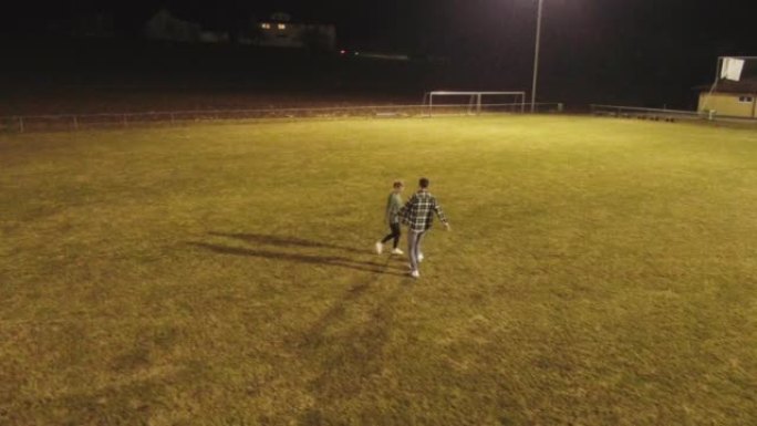 空中无人机拍摄了两个人在夜间在田野里踢足球的镜头