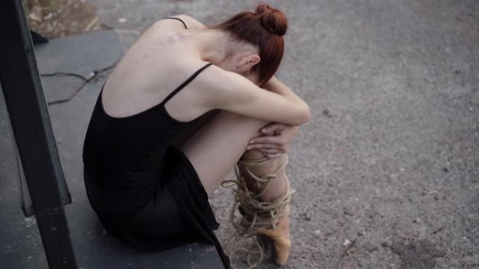 压力大的年轻女子的顶角视图，坐着拥抱膝盖。沮丧的苗条的白人芭蕾舞女演员，腿上系着绳子。束缚沮丧的舞者