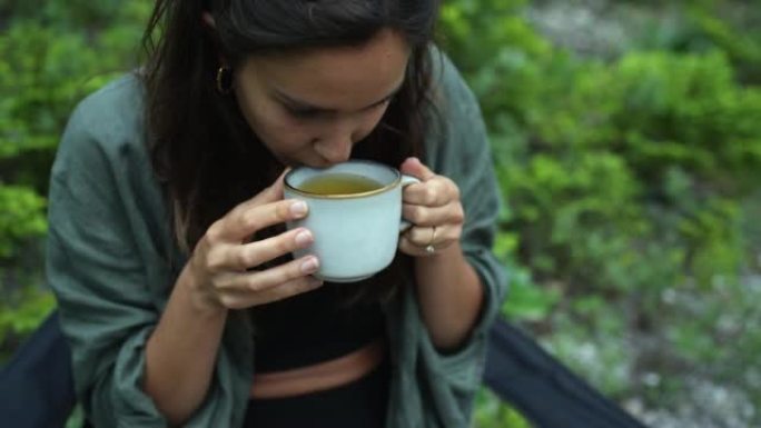 露营椅上的女人在森林里喝热饮料的细节