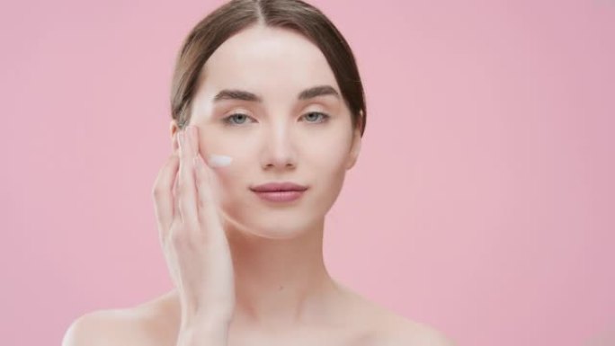 苗条的年轻女子把面部护理霜在她的脸颊上笑得大大的