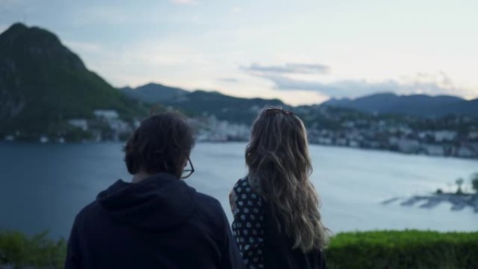 夫妻俩坐在长凳上俯瞰日落时卢加诺湖