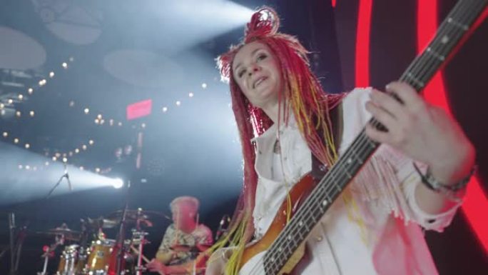 在当代音乐音乐会上，戴着粉色辫子的有趣女人在舞台上弹吉他