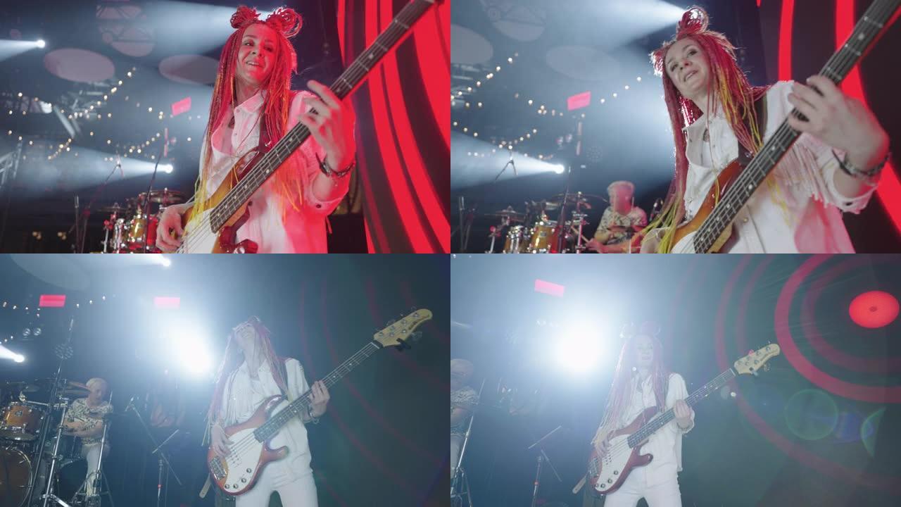 在当代音乐音乐会上，戴着粉色辫子的有趣女人在舞台上弹吉他