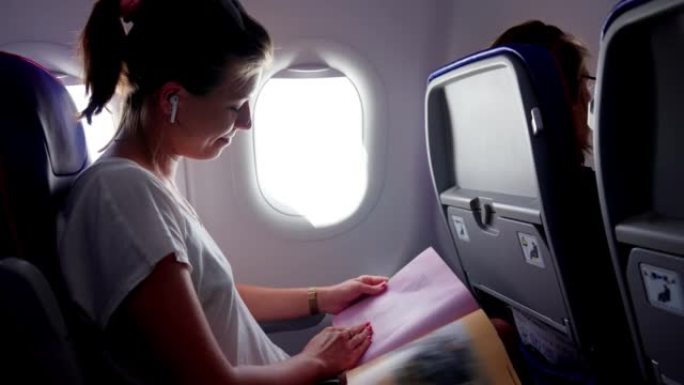 戴耳机的年轻女子在飞机上看书。