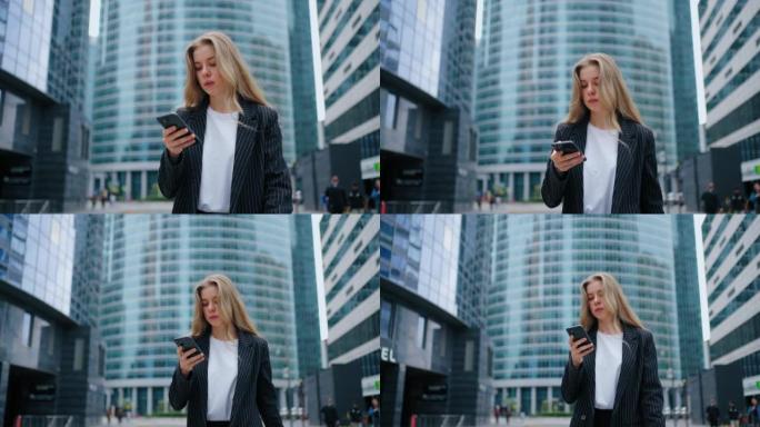 在摩天大楼的背景下，一个年轻的女人走在大都市的街道上，手里拿着手机，一边看新闻一边做生意