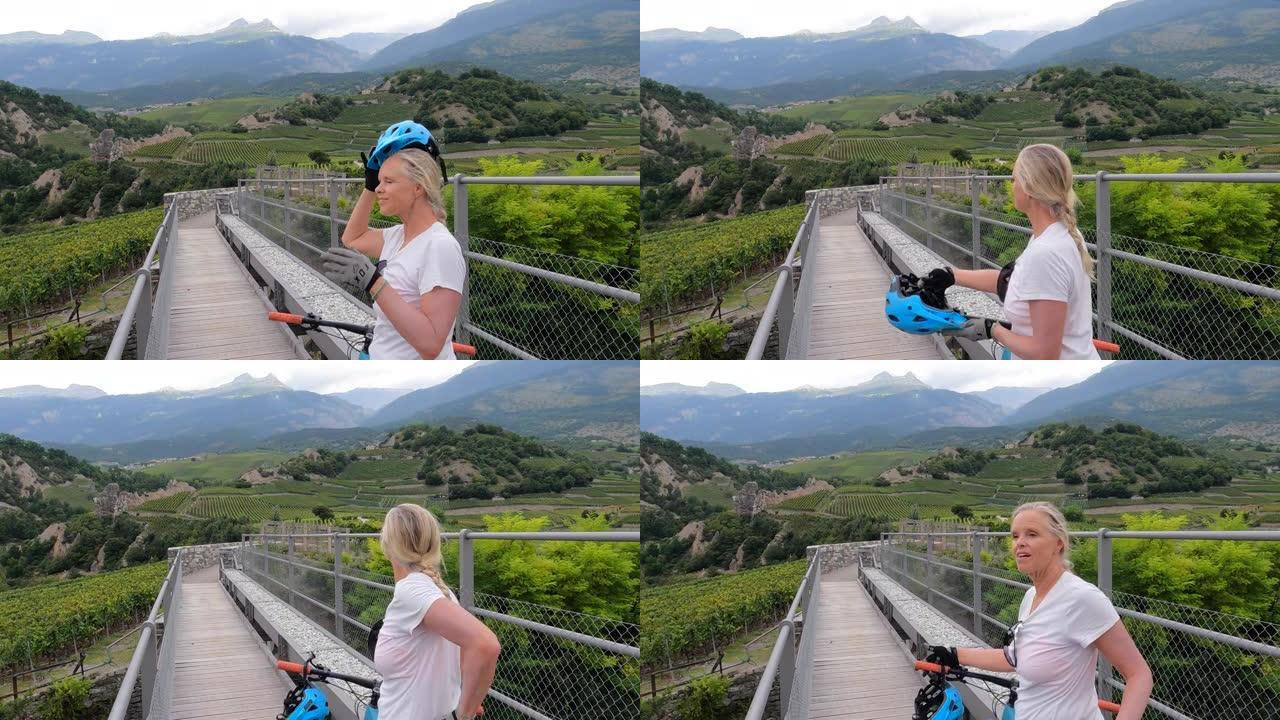 成熟的女人自行车穿过葡萄园和山脉