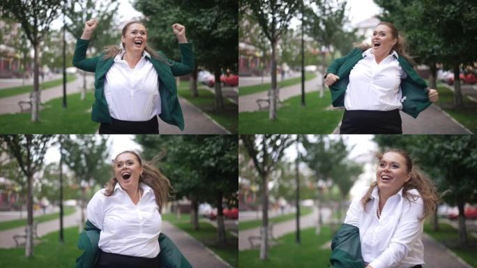 快乐快乐的超重女人尖叫着高兴地站在城市街道上，以慢动作脱下夹克。前视图中等镜头快乐的高加索肥胖成功女