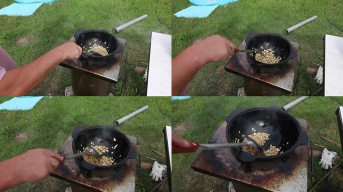 一个男人在铸铁大锅里炸洋葱。在户外准备食物。