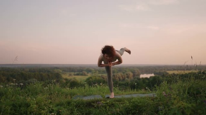 一名年轻女子通过在大自然的地毯上做瑜伽练习来保持平衡在背景中滑翔伞跳伞运动员正在慢动作飞行