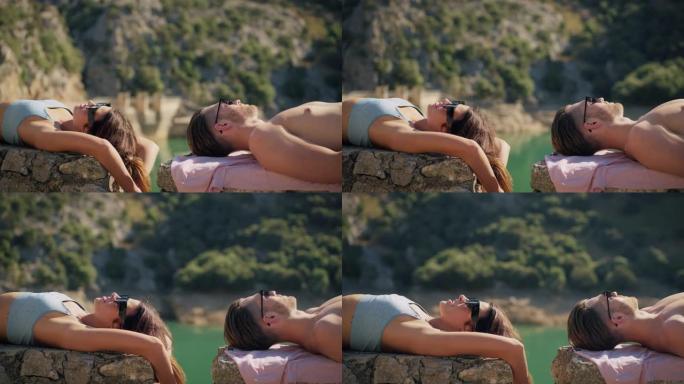 浪漫的情侣在碧绿的湖边的石栅栏上晒日光浴。