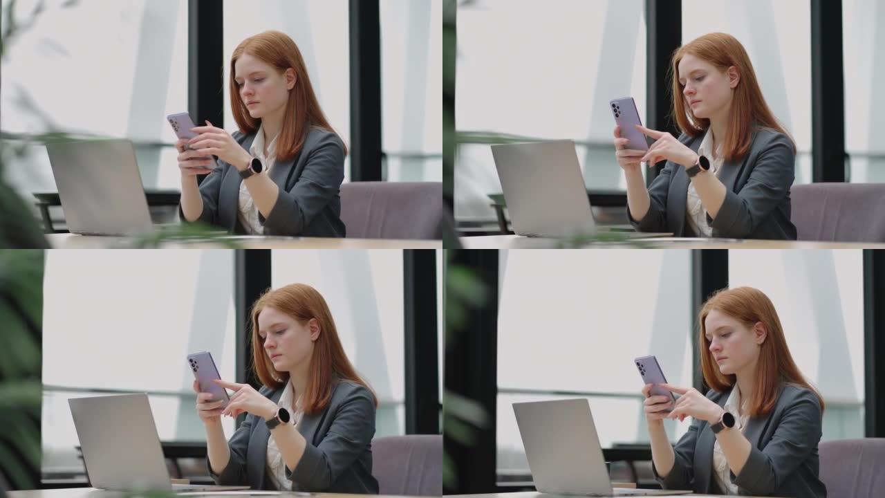 年轻的女商人使用带笔记本电脑的智能手机。商务女性在一个现代办公室，有一个全景窗口，阳光明媚的日子，笔