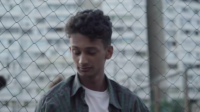悲伤的非洲裔美国少年的特写肖像，回头看着踢足球的家伙，然后转身离开。不幸的年轻人坐在城市摩天大楼背景