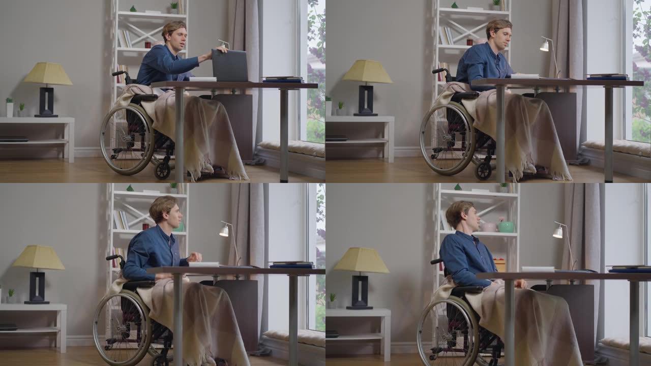 宽镜头满意的残疾人坐在轮椅上关闭笔记本电脑，看着窗外。自信的高加索瘫痪的自由职业者在家慢动作在线工作