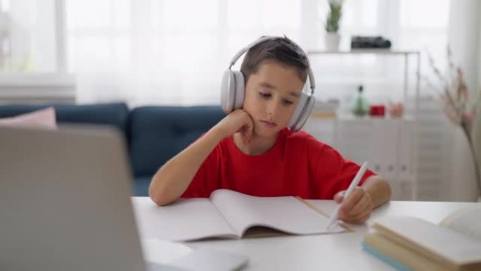 戴着耳机的男生不想学习，坐在家里的办公桌前