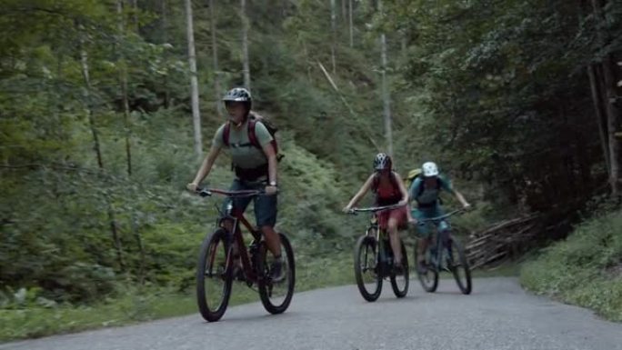 三名女山地车手一起骑在树林中的铺砌道路上