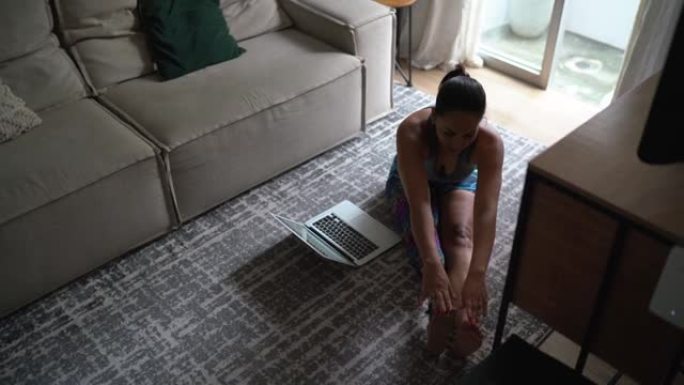 残疾妇女在家里看笔记本电脑上的健身课时伸展身体