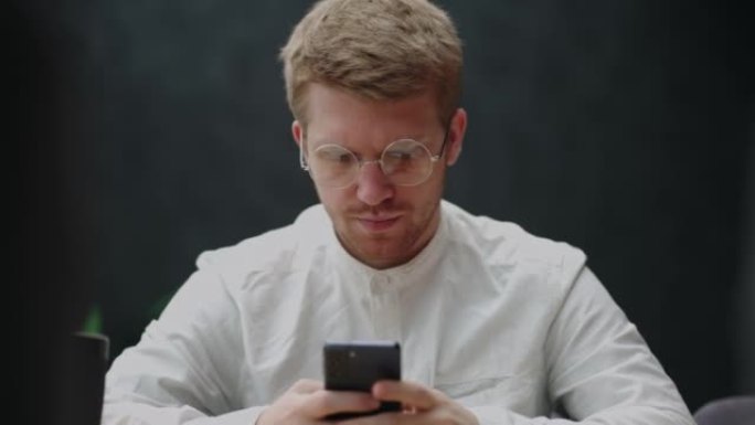 穿着白衬衫，戴着眼镜的聪明帅哥正在使用现代手机，查看社交媒体