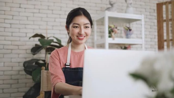 穿着围裙的亚洲妇女使用笔记本电脑工作