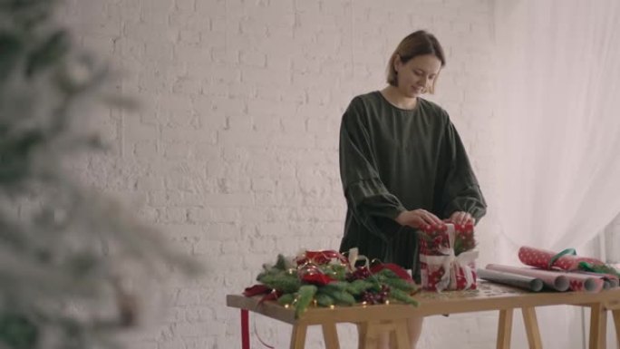 礼物包装纸的女孩装饰者的肖像站在桌子旁，装饰着礼物包装纸，圣诞节树枝和丝带