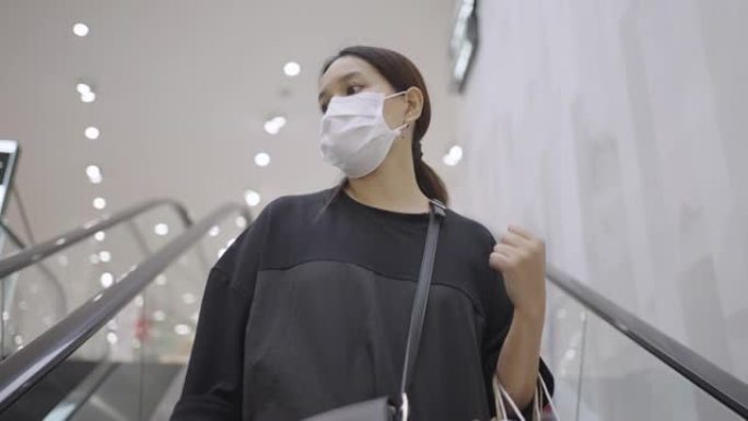 戴口罩的女人在购物中心的自动扶梯上向下移动