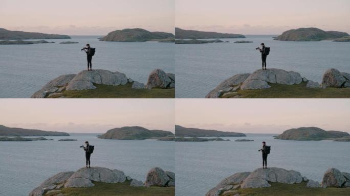 摄影师站在海湾上方的岩石露头上的广阔视野，背后是山脉