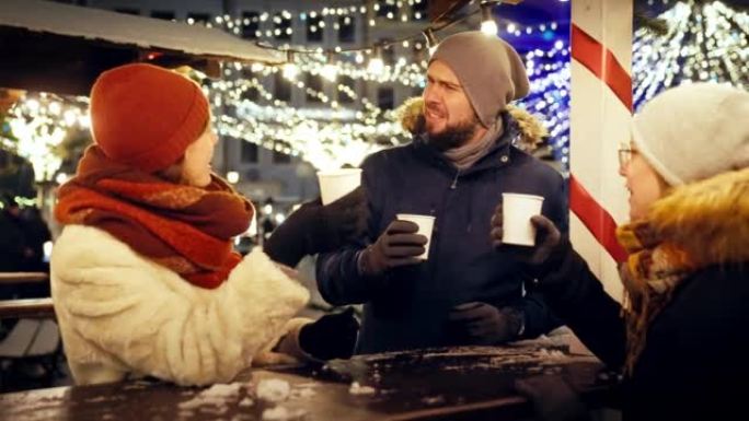 一群朋友在慢动作的下雪的圣诞节夜晚一起用热巧克力敬酒
