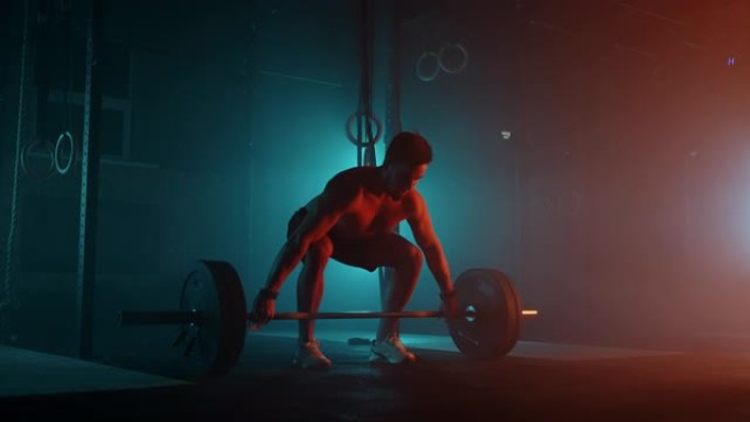 蓝色橙色霓虹灯下的男性举重运动员正在准备在健身房锻炼。一个身体裸露的强壮男人确实将杠铃举过头顶，这是