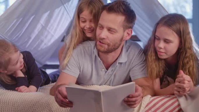 父亲和女儿一起在舒适的天篷床上度过时光。阅读书籍