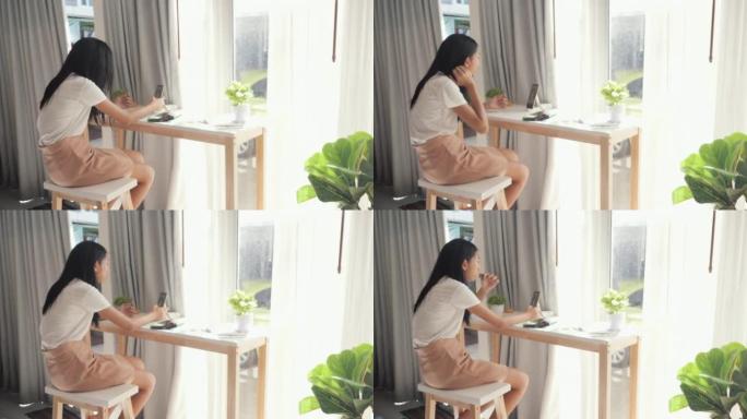 亚洲女孩通过智能手机观看电影或病毒视频，并在周末在家的窗户附近吃脆皮海藻。