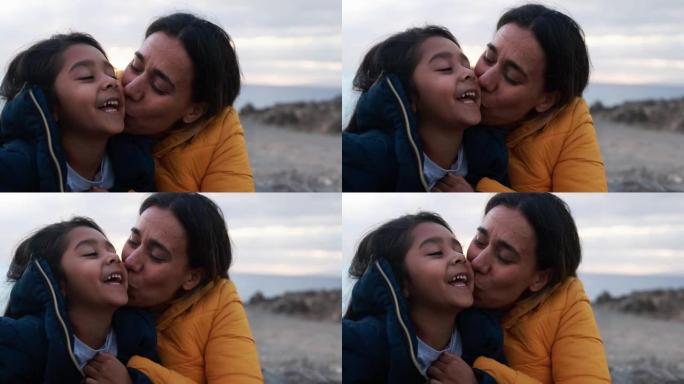 拉丁母亲在冬天日落时与女儿在海滩上的温柔时刻