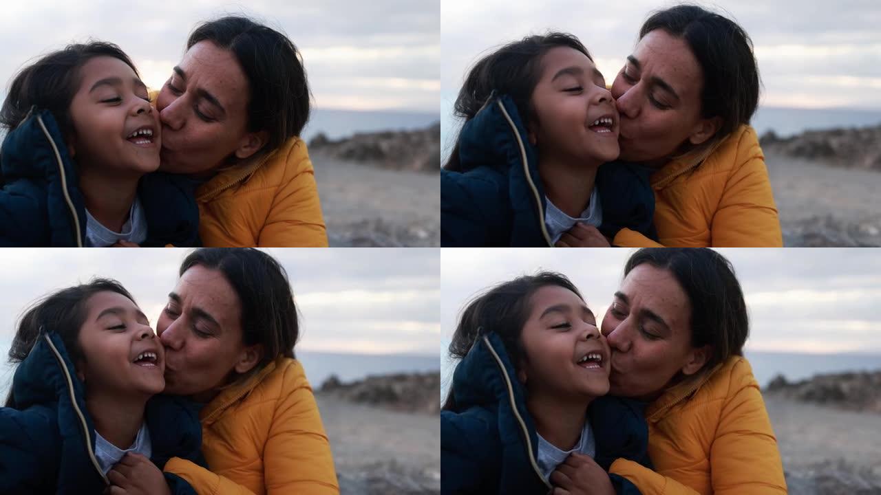 拉丁母亲在冬天日落时与女儿在海滩上的温柔时刻