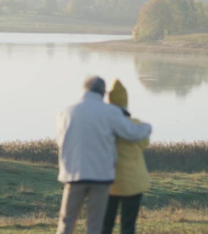 慈爱的老年夫妇在湖边拥抱，欣赏垂直视频