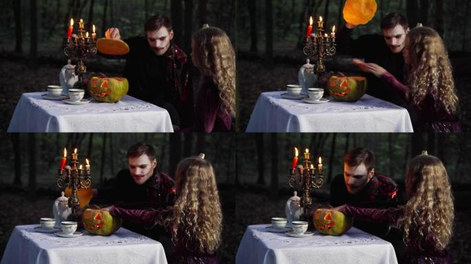 万圣节期间，小漂亮女孩和穿着吸血鬼服装的男人坐在黑暗的森林里，用蜡烛打开蔬菜。快乐的高加索兄妹庆祝。