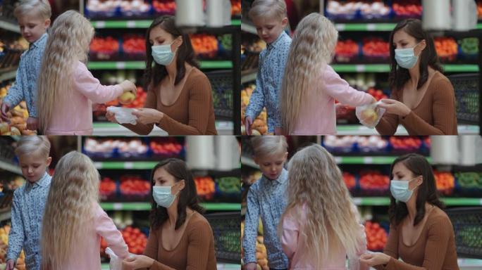 一位戴着防护面具的母亲带着两个孩子正在超市买杂货。与孩子一起购买食品蔬菜和水果