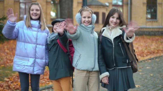 一群积极的青少年学生挥舞着微笑，看着秋天站在户外的相机。快乐开朗的高加索男孩和女孩在校园里摆姿势。回
