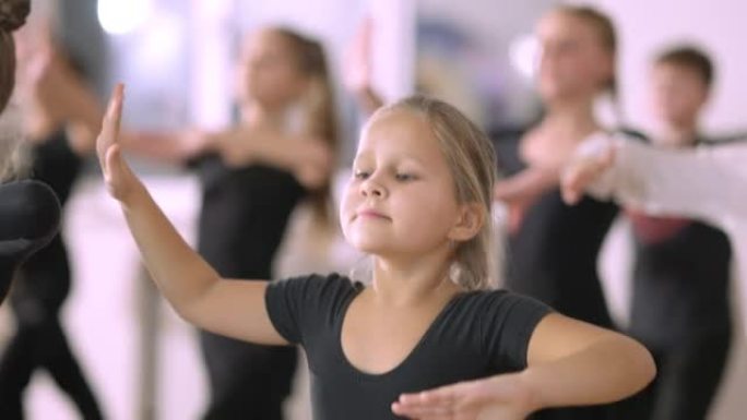 相当严肃的小女孩在舞蹈工作室的第四个芭蕾舞位置迈出了一步。才华横溢的高加索儿童在舞蹈学校背景下与孩子