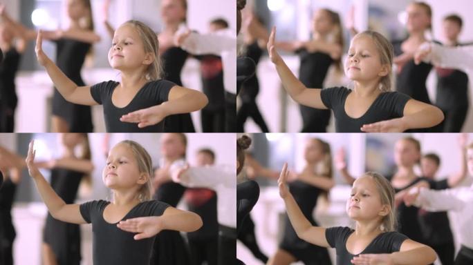 相当严肃的小女孩在舞蹈工作室的第四个芭蕾舞位置迈出了一步。才华横溢的高加索儿童在舞蹈学校背景下与孩子